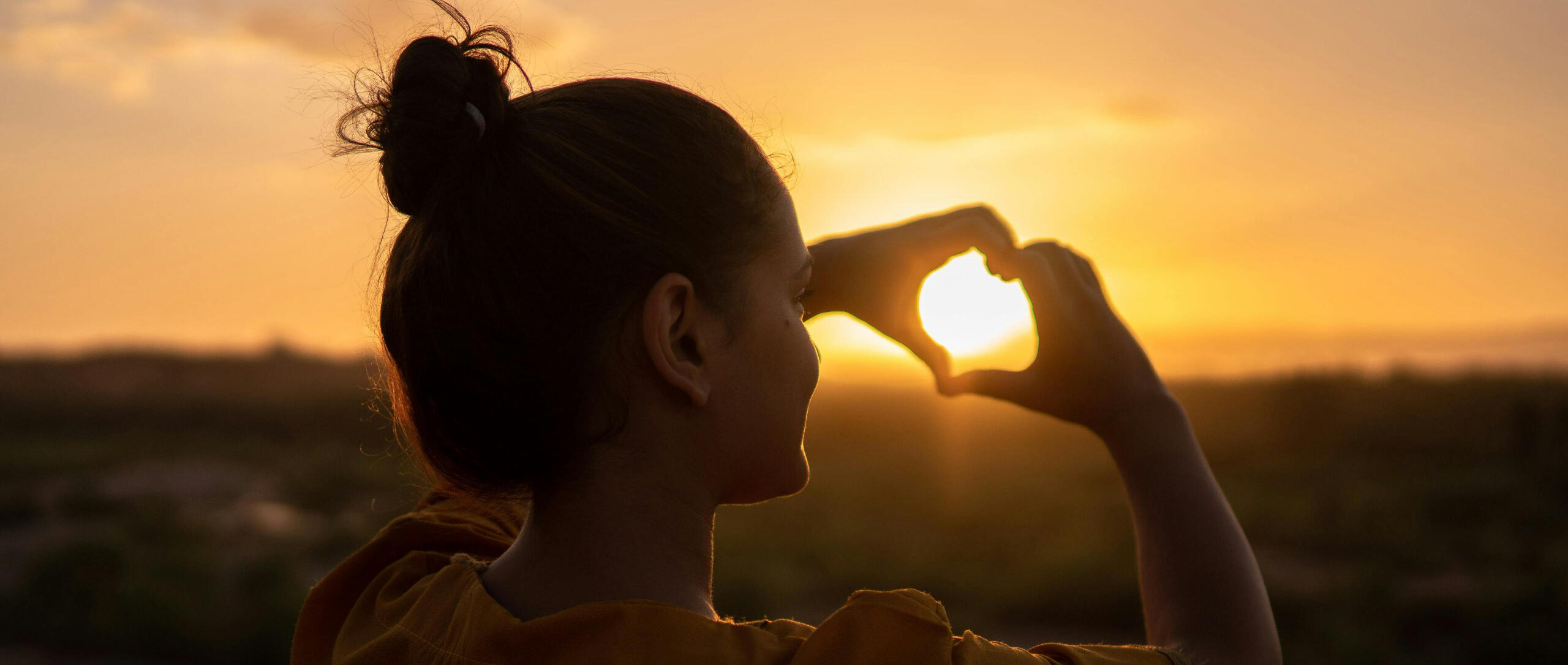 Woman forming a heart shape with her hands at sunset, symbolising community and shared support.